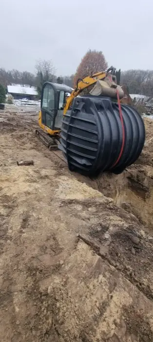 Bagger setzt Zisterne in Baugrube